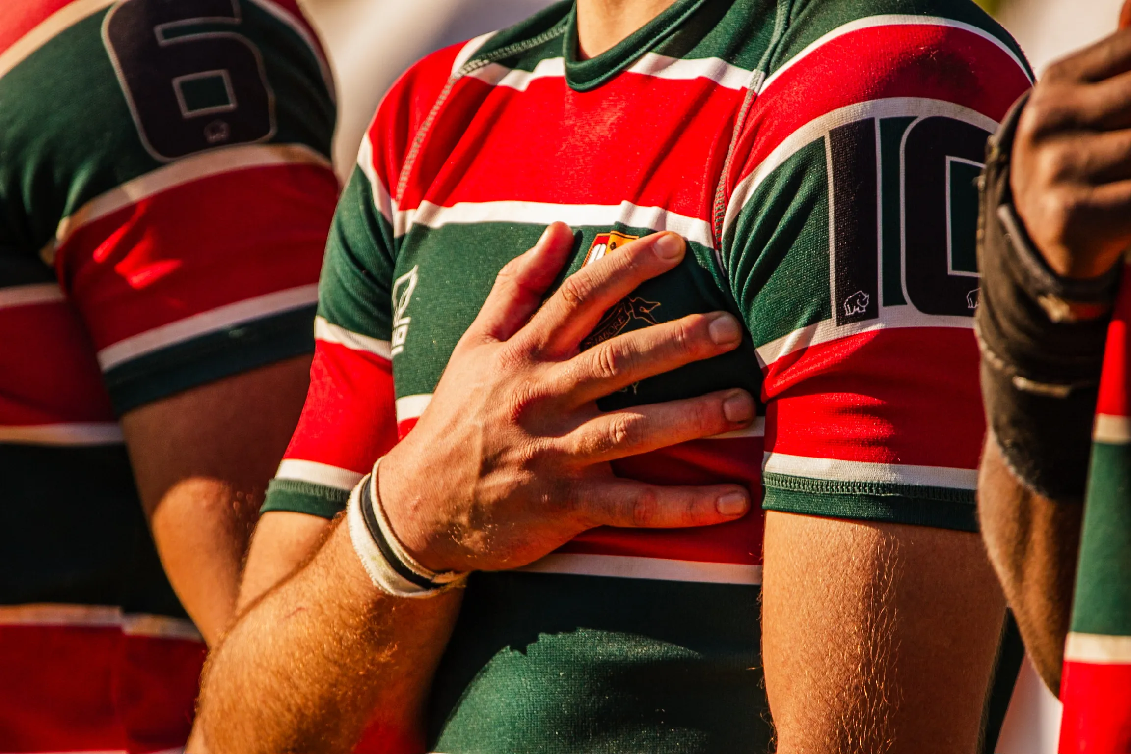 A close detail of striped rugby jerseys, a player's hand pressed to his chest before kick-off.