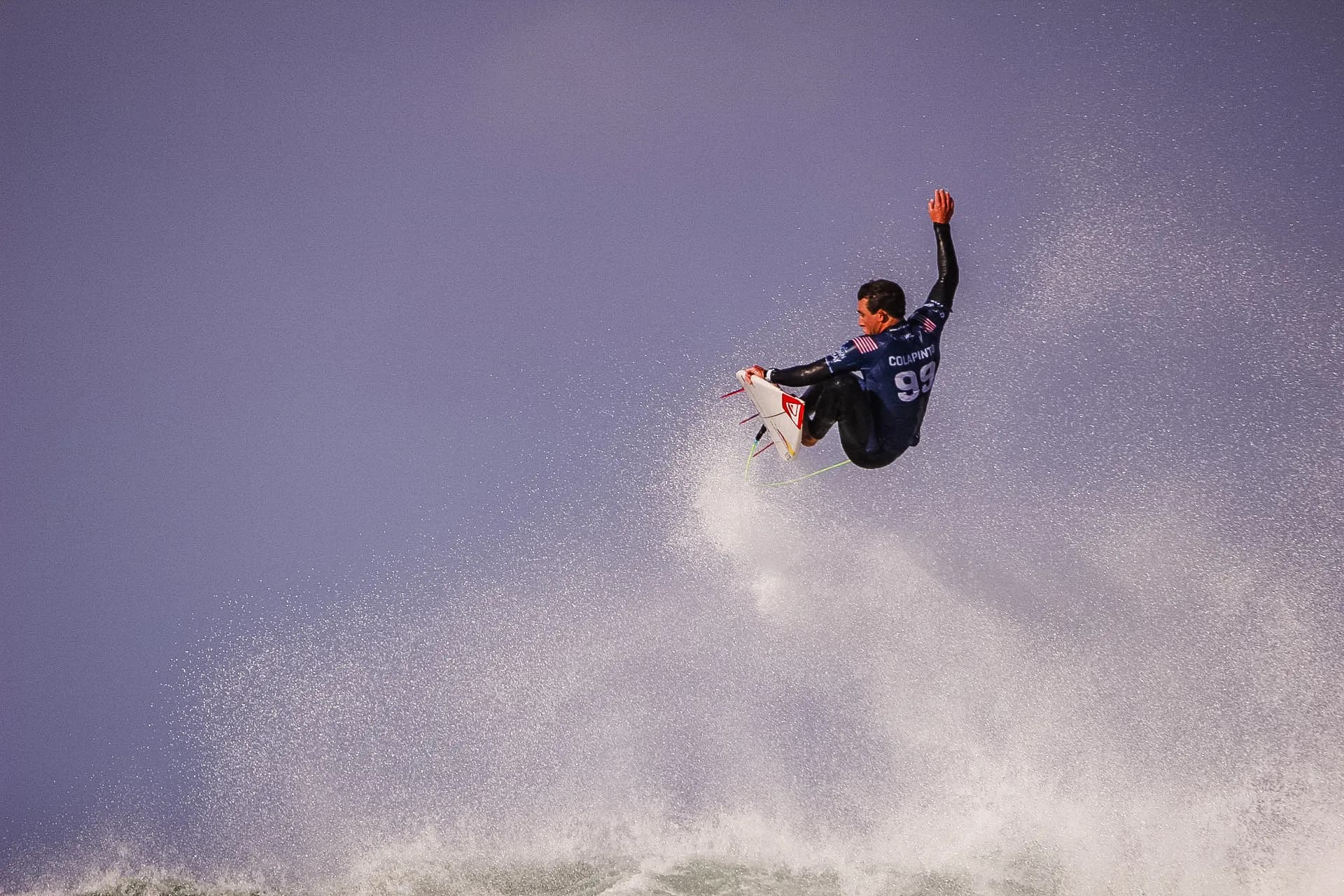 A surfer launching a full aerial above the wave, silhouetted against a wash of spray.